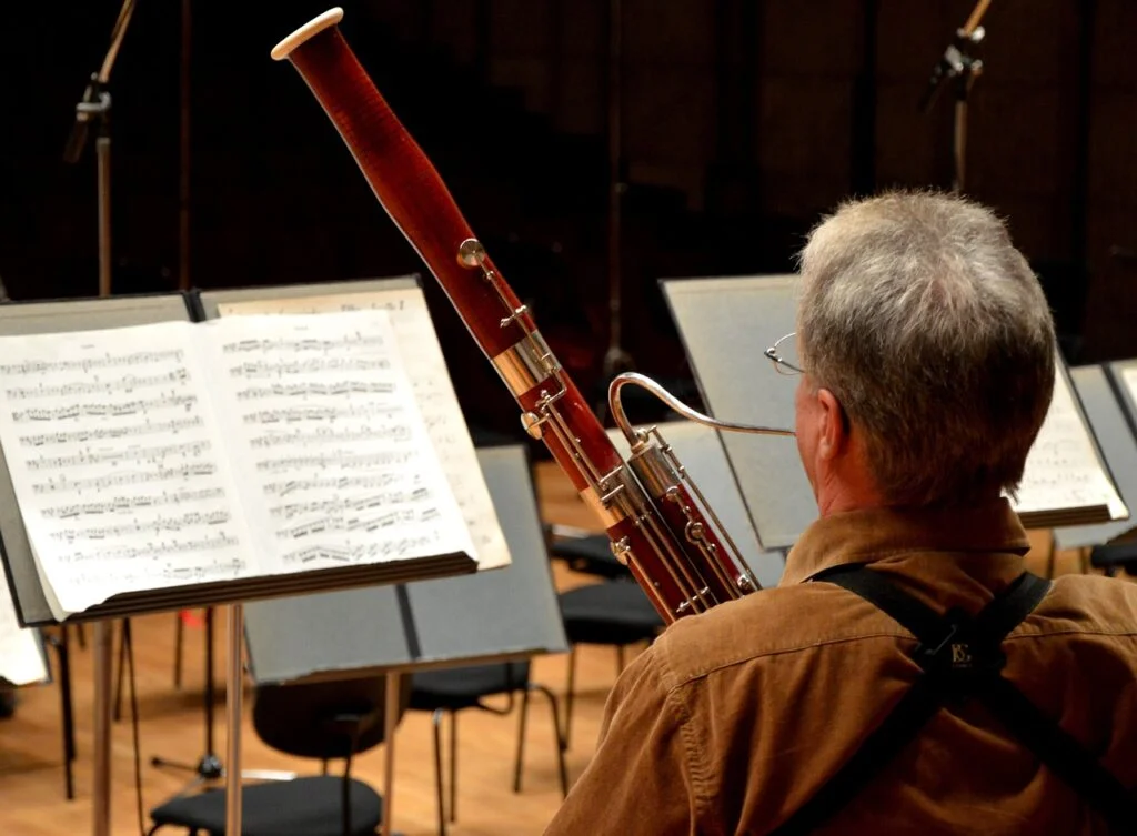 A bassoon player seated in front of sheet music on a stand