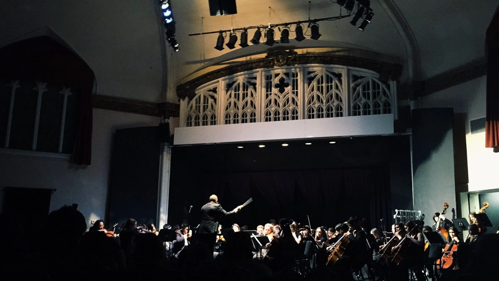 An orchestra and conductor performing on a lit stage in a concert hall